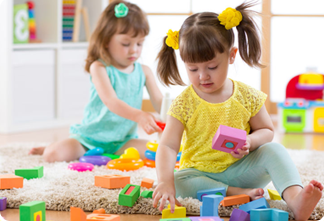 Two little girls playing with blocks on the floor.